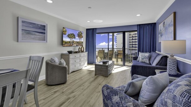A modern living room with a balcony, a dining area, and a view of the city skyline. - Bluewater Resort V408A (Myrtle Beach)