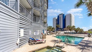 A pool area with lounge chairs, a small pool, and a building with balconies. - Bluewater Resort V408A (Myrtle Beach)