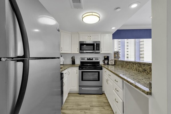 A modern kitchen with white cabinets, stainless steel appliances, granite countertops, and a window with blinds.