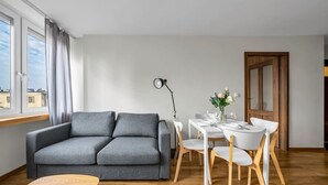 Ein modernes Wohnzimmer mit grauem Sofa, einem Holztisch und einem Essbereich mit weißen Stühlen und einem kleinen Tisch.