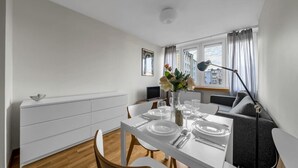 Ein moderner Essbereich mit einem weißen Tisch für vier Personen, einer Blumenvase und Blick auf die Stadt durch das Fenster.