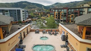A rooftop pool area with lounge chairs and a hot tub, surrounded by multi-story buildings with balconies.