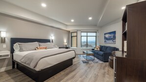 A modern hotel room with a large bed, a sofa, a desk, and a view of the city.