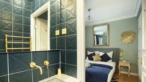 Une salle de bain moderne avec une grande baignoire, une douche et des toilettes. La pièce adjacente contient un lit recouvert d’une couverture bleue et agrémenté d’oreillers.