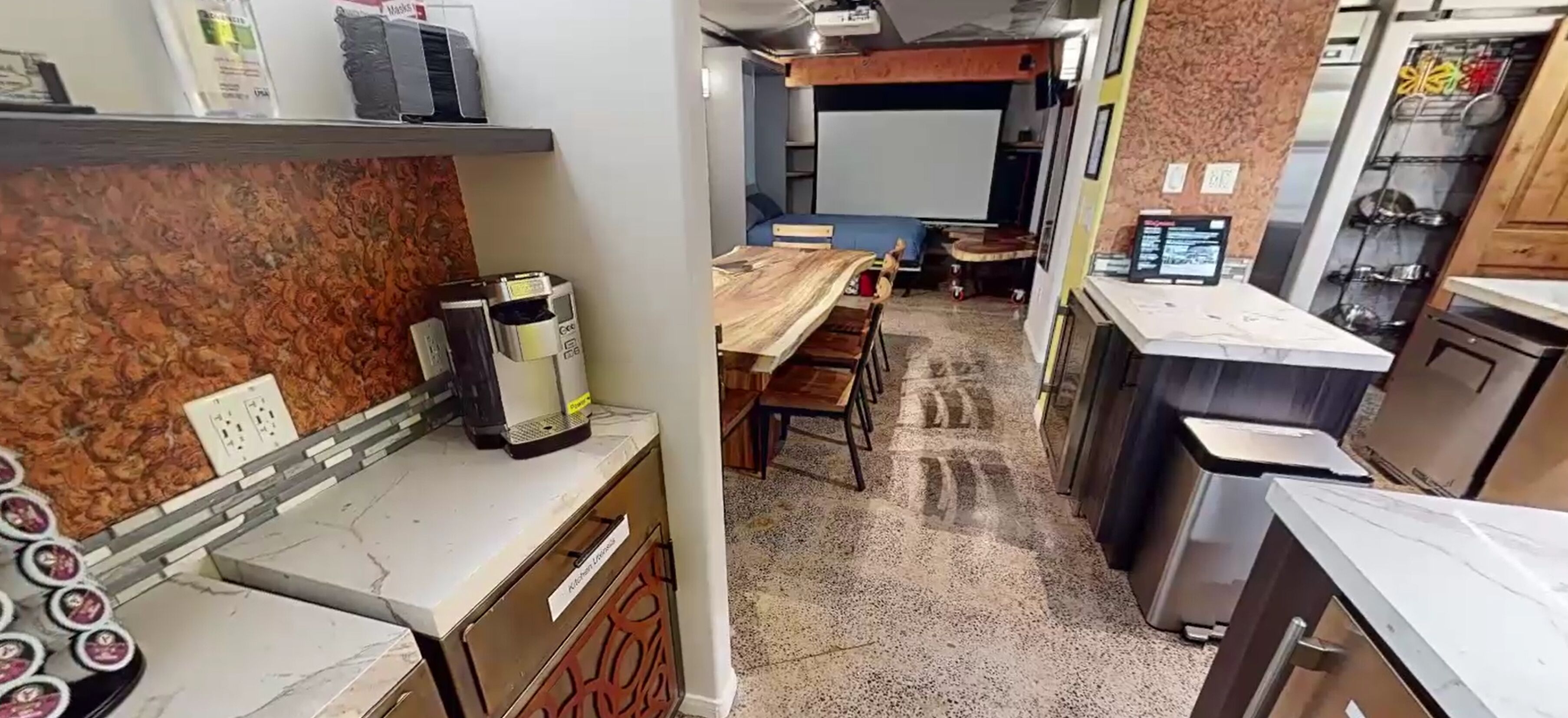 A compact kitchen with a coffee machine, a dining area with a table and chairs, and a small seating area with a screen.