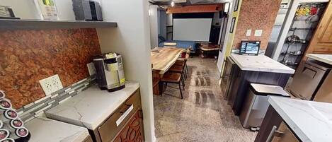 A compact kitchen with a coffee machine, a dining area with a table and chairs, and a small seating area with a screen.