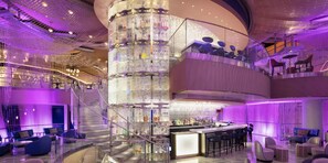 Un moderno vestíbulo de hotel con una escalera espiral central, zona de bar y diferentes disposiciones de asientos.