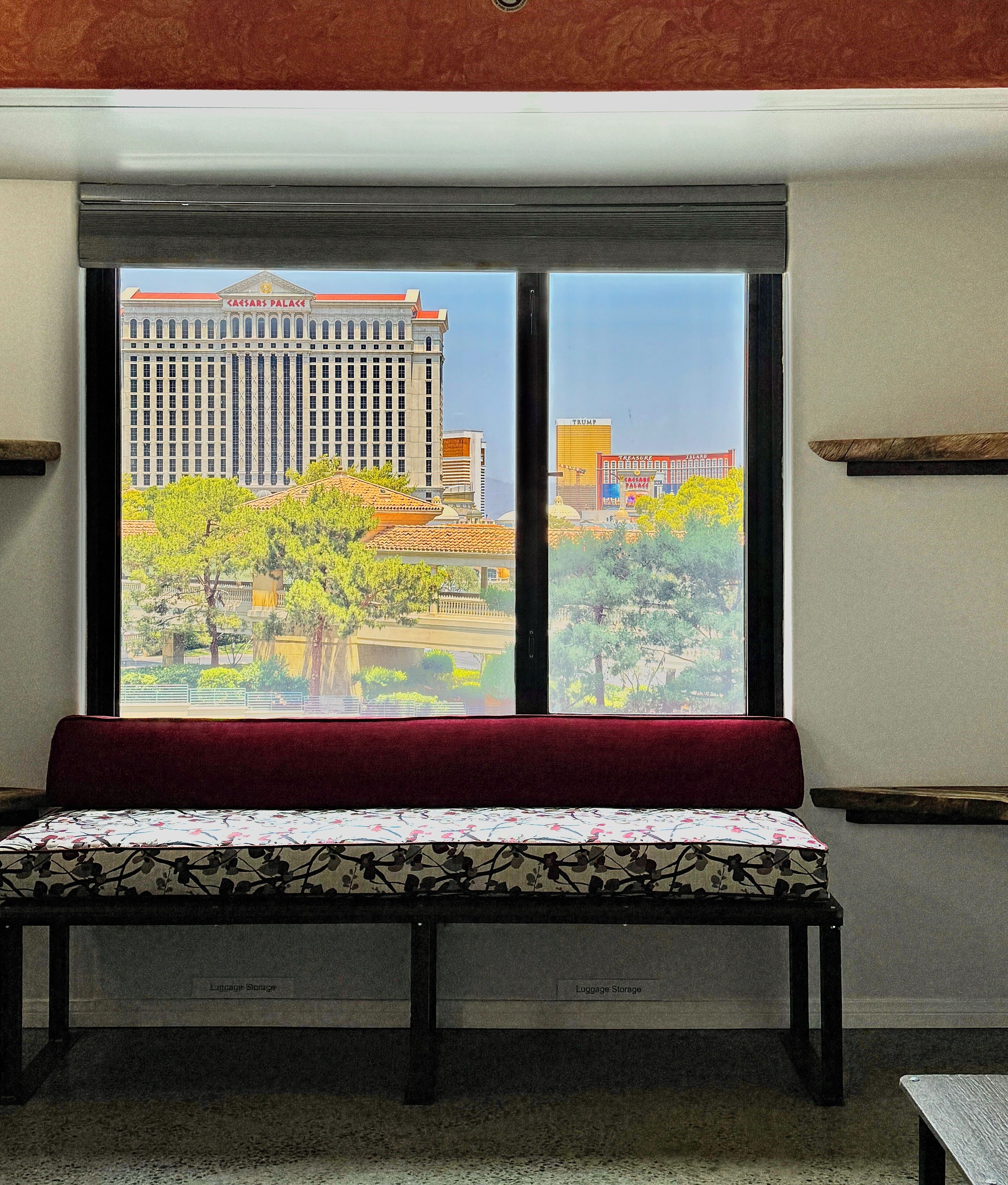 Un banco con cojín floral en una habitación con un ventanal que da a un paisaje urbano.