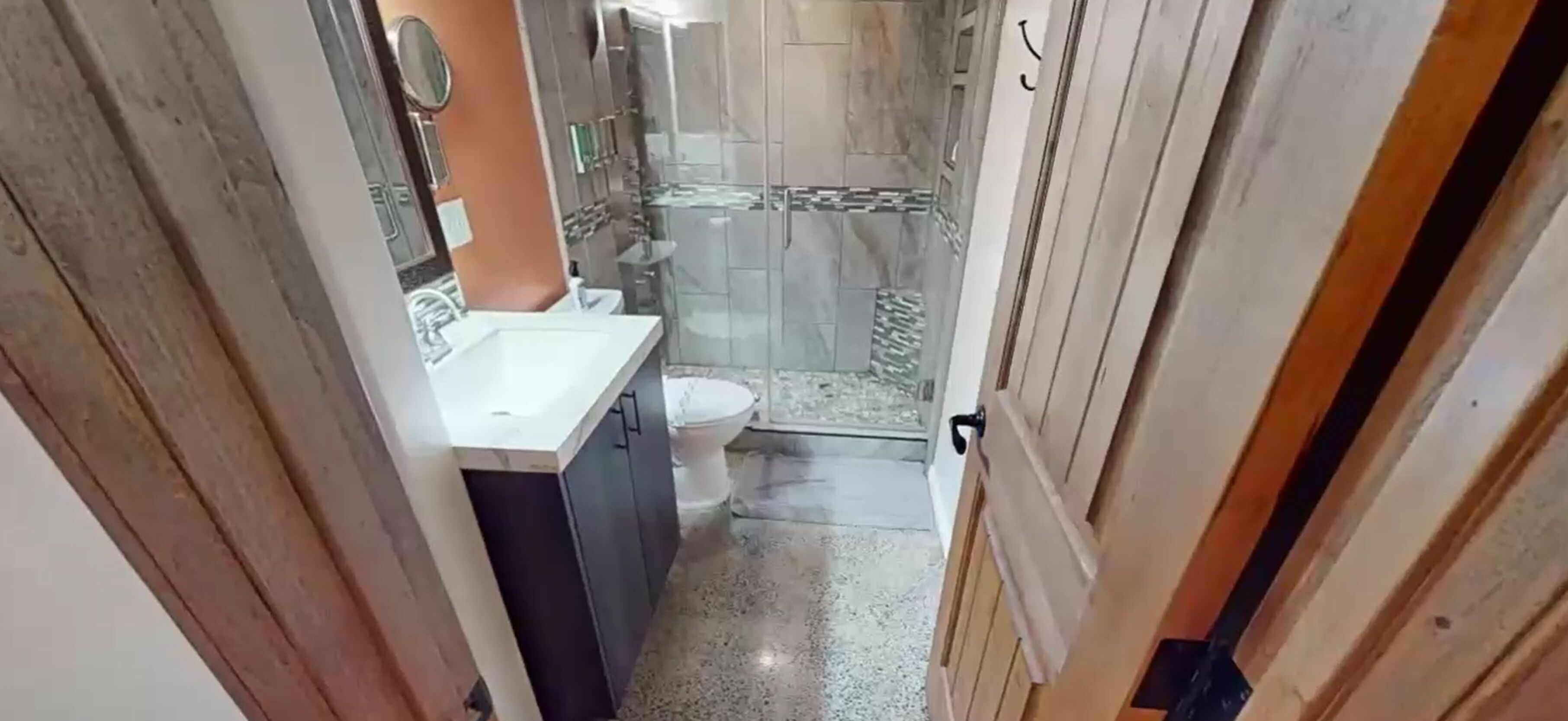 Ein schmaler Flur, der zu einem Badezimmer mit Toilette, Waschbecken und Duschbereich führt.