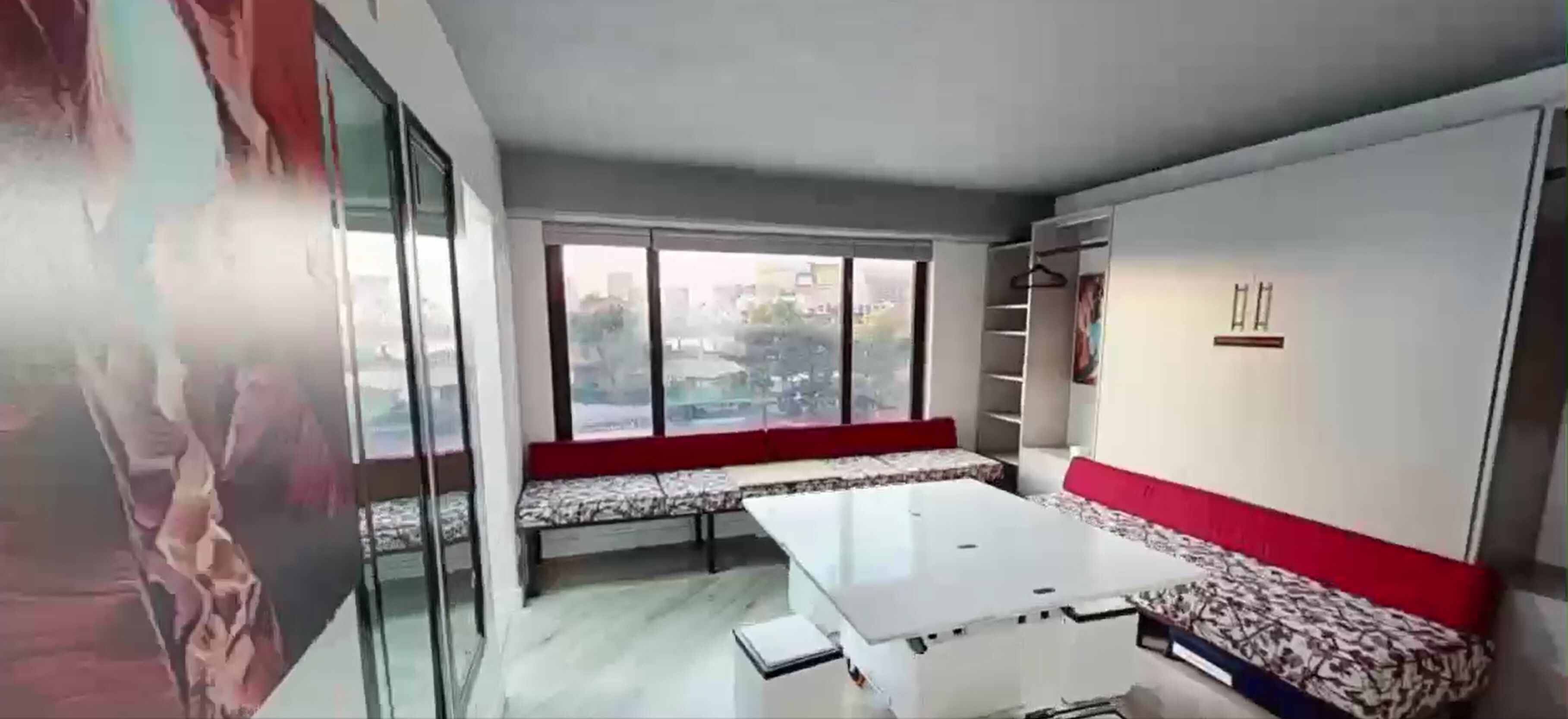 Ein modernes Zimmer mit großem Fenster, einer Couch, einem Tisch und einem Kleiderschrank.
