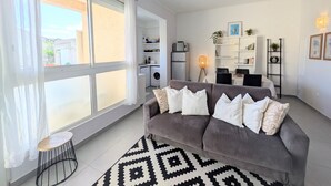 A modern living room with a grey sofa, white cushions, a patterned rug, and a dining area with a table and chairs. - La Perla di Santa Maria - Vue mer, plage à 100 m (Santa-Maria-Poggio)