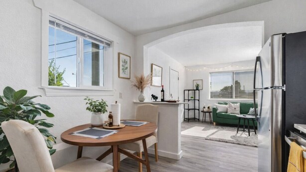 A modern living room with a dining area, a green sofa, and a kitchen with a refrigerator.