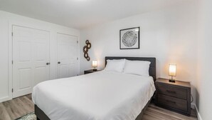 A bedroom with a bed, two bedside tables, a wall-mounted light fixture, and a door.