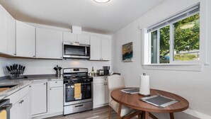 A compact kitchen with white cabinets, a microwave, stove, and a dining area with a round table and chairs.