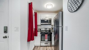 Una cocina compacta con armarios blancos, un refrigerador de acero inoxidable, un microondas y un horno.