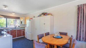 Cocina compacta con comedor, que incluye una mesa redonda de madera con cuatro sillas, un refrigerador y una ventana que proporciona luz natural.