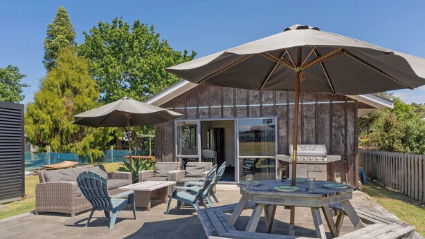 Un patio al aire libre con una mesa y sillas de madera, un paraguas grande y una parrilla.
