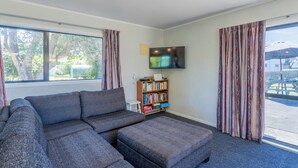 Una sala de estar moderna con un sofá modular, un televisor de pantalla plana, una estantería y ventanas amplias con cortinas.