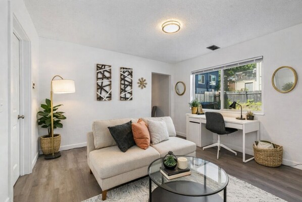 A living room with a sofa, coffee table, desk, and a large window.