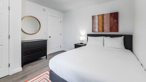 A bedroom with a bed, a bedside table with a lamp, a dresser, a round mirror, and a painting on the wall. - Lovely Remodeled 1BR in DT Tacoma - 6 (Tacoma)