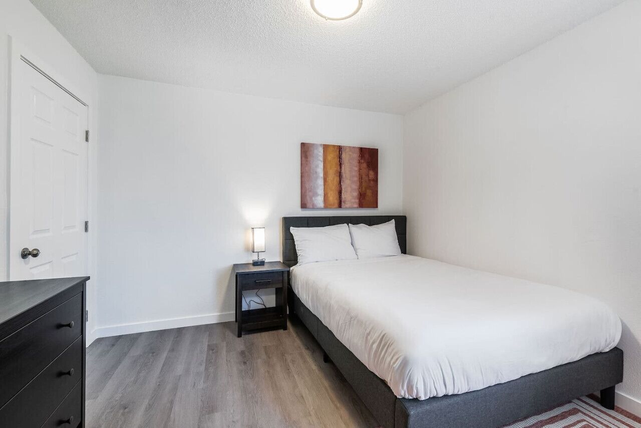 A bedroom with a bed, nightstand, dresser, and a painting on the wall.