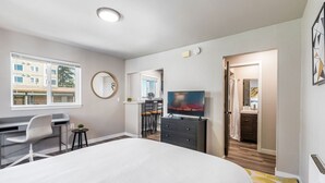 A modern hotel room with a large bed, a desk, a chair, a TV, and a bathroom visible through an open door.