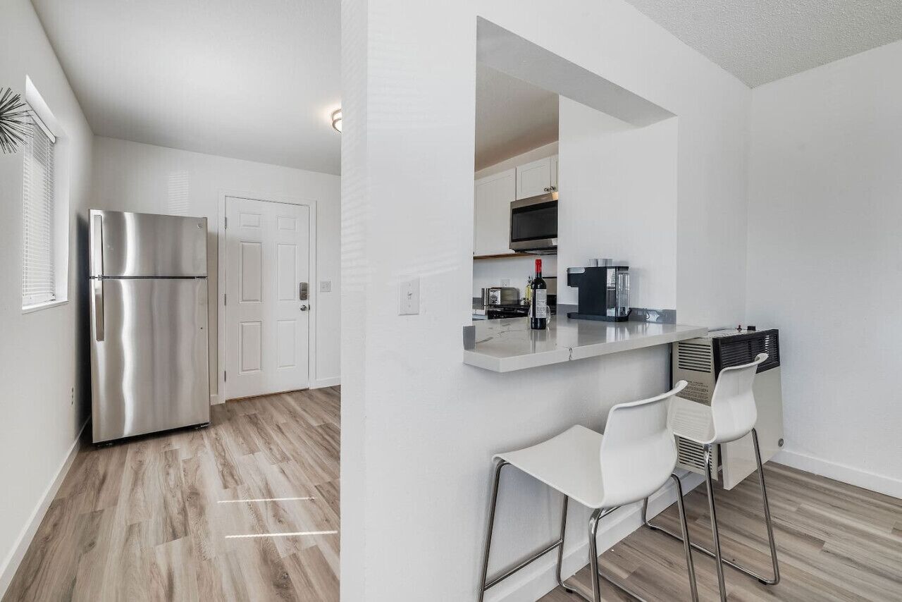 A modern kitchen with a stainless steel refrigerator, white cabinets, and a bar area with white chairs.