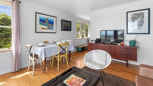 A modern living room with a dining area, wooden flooring, and a large window with curtains.