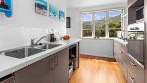 A modern kitchen with a large window, stainless steel appliances, and wooden flooring.