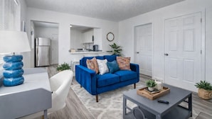 A modern living room with a blue sofa, white armchair, and a coffee table. There is a kitchen in the background with a refrigerator and a microwave. - Fresh 1BR/1BA in Downtown Tacoma - 2 (Tacoma)