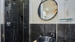 A bathroom with a black marble shower, a round mirror, and a sink with a wooden countertop.
