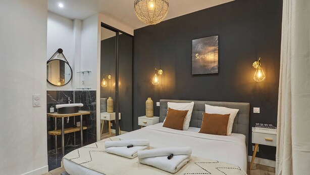 A modern bedroom with a large bed, bedside tables, a mirror, and wall-mounted lighting.
