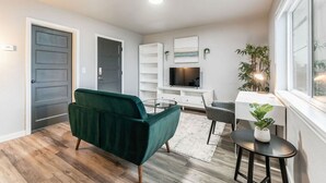 A modern living room with a green armchair, a glass coffee table, a white TV stand, and a small side table with a plant.