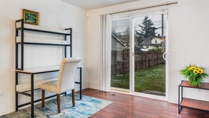 Habitación con escritorio, silla y vista al jardín trasero a través de un ventanal corredizo.