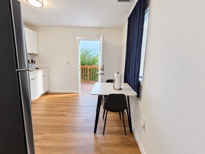 A compact kitchen with a dining area, a refrigerator, and a window with curtains.