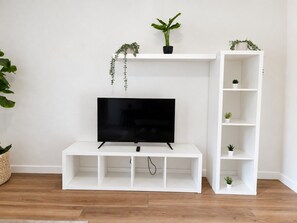 Un meuble de rangement blanc pour appareils multimédias, avec un téléviseur à écran plat, des étagères et des plantes en pot.