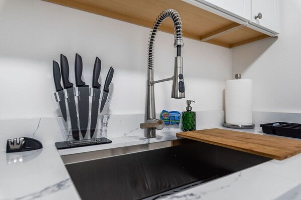 A kitchen with a stainless steel sink, a knife block, a soap dispenser, and a roll of paper towels.
