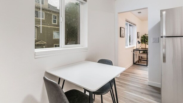 A modern kitchen with a white table and chairs, a stainless steel refrigerator, and a window overlooking a residential area.