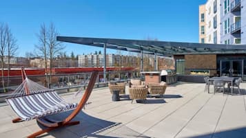 Een terras op het dak met een hangmat, rieten meubilair en een vuurplaats.