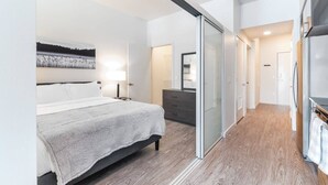 Un dormitorio moderno con cama, cómoda y puerta corredera de vidrio que da a un baño.