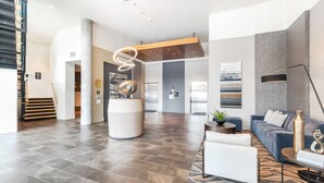Un vestíbulo amplio y de diseño moderno, con un área de estar central con sofás y una mesa de centro, una escalera a la izquierda y un pilar con una lámpara de diseño único.