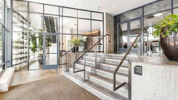 Een moderne hotellobby met een glazen ingang, een trap met metalen leuningen en een grote kamerplant.
