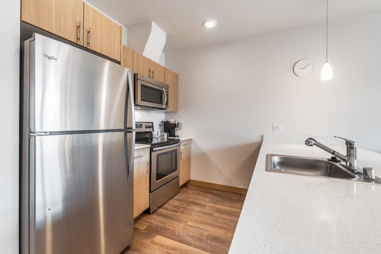 A modern kitchen with stainless steel appliances, wooden cabinets, and a white countertop.