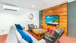 Ein modernes Wohnzimmer mit grauem Sofa, einem Holztisch, einem an einer Holzwand montierten Fernseher und einem Kunstwerk an der Wand.