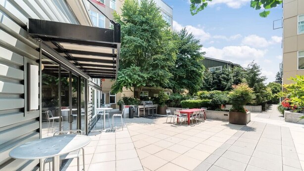 Ein Terrassenbereich im Freien mit Tischen, Stühlen, einem Grill und Kübelpflanzen.