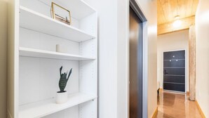 A hallway with white shelves, a potted plant, and a door with a dark panel.