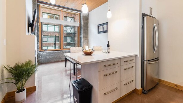 A modern kitchen with a central island, stainless steel refrigerator, and pendant lighting.