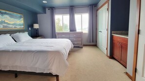 A bedroom with a bed, a dresser, a nightstand, and a window with curtains.