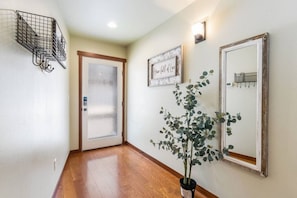 A hallway with a wooden floor, a frosted glass door, a potted plant, and a mirror on the wall.