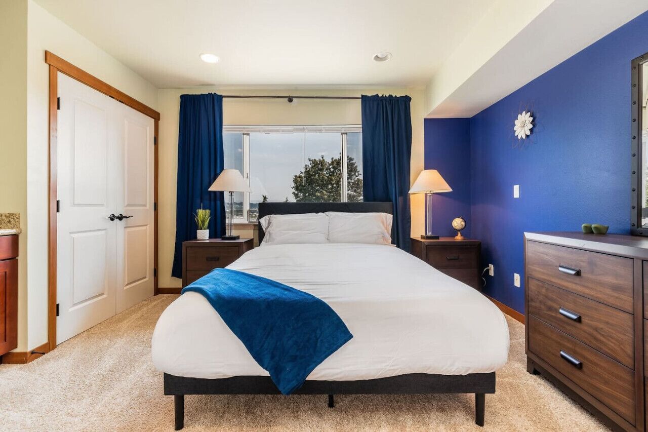 Un dormitorio con una cama, dos mesitas de noche, un tocador y una ventana con cortinas.